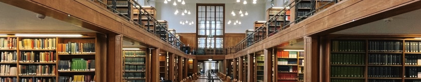 Shows one of the wings of the Wills Memorial Library. A large wood panelled library on two floors, with book shelf alcoves with large empty study desks